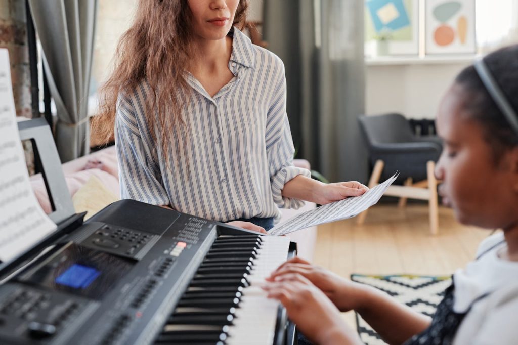 A child learns piano at home with her teacher offering guidance and support.