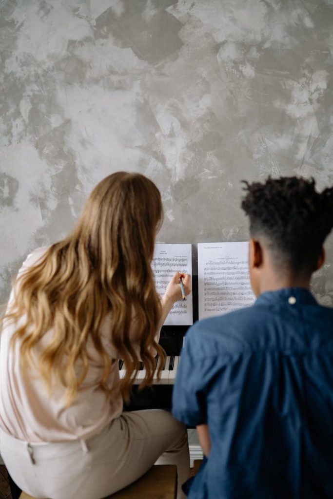 Back view of a woman teaching a child piano, focusing on musical notes.